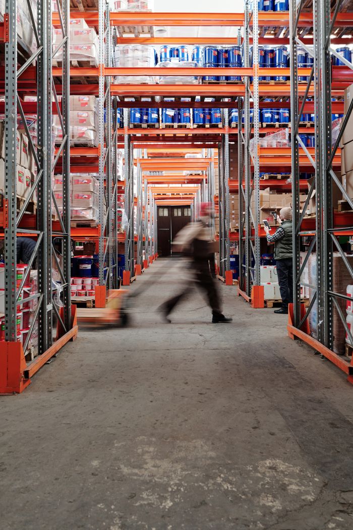 pexels-photo-4483859 Blurred motion of a man walking in a spacious warehouse aisle between tall shelves.